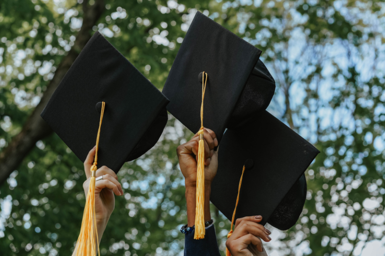 Three students holding up graduation caps